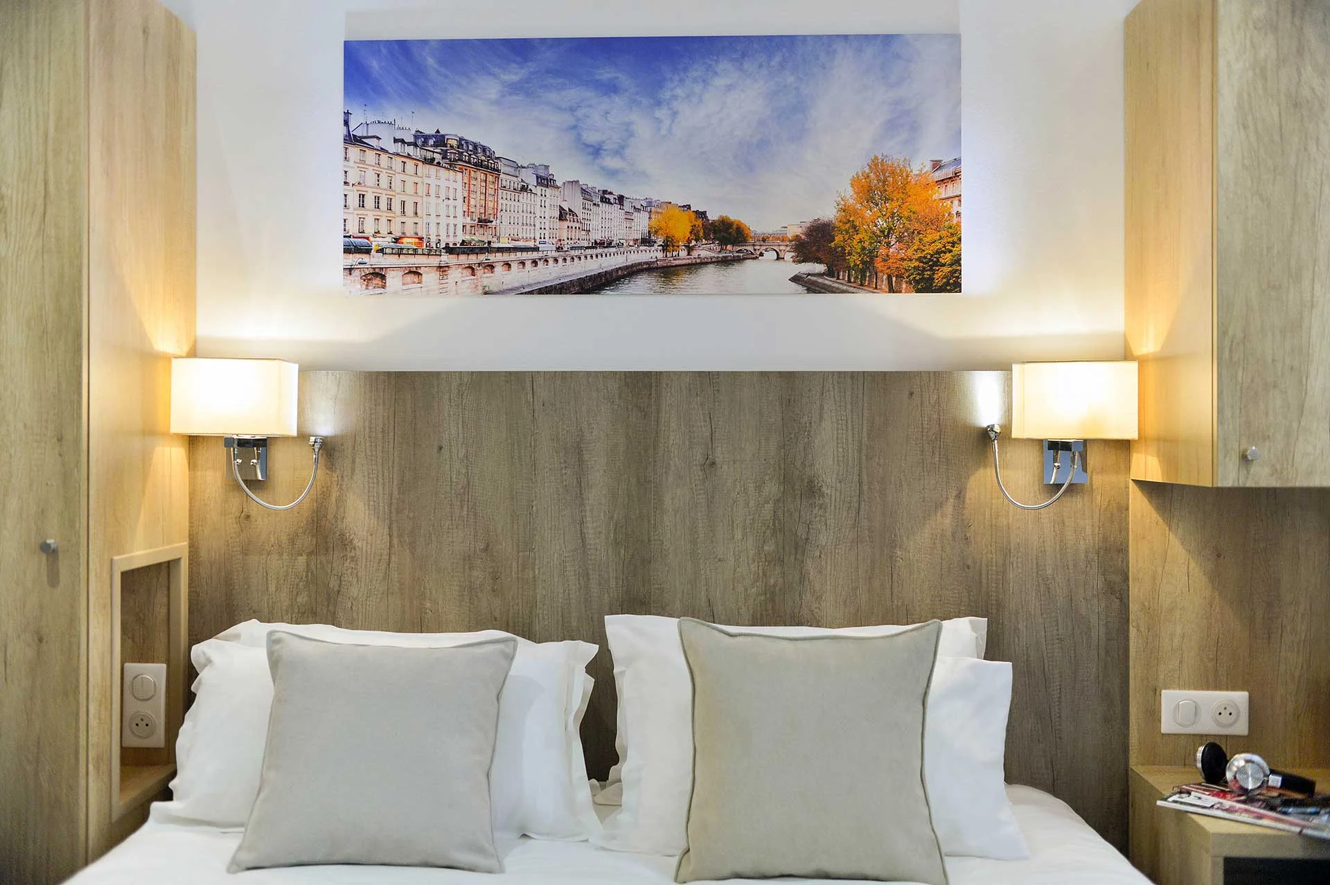 Lit de nos chambre Standard Double avec drap blanc, meuble en bois et tableau de paris sur le murs.