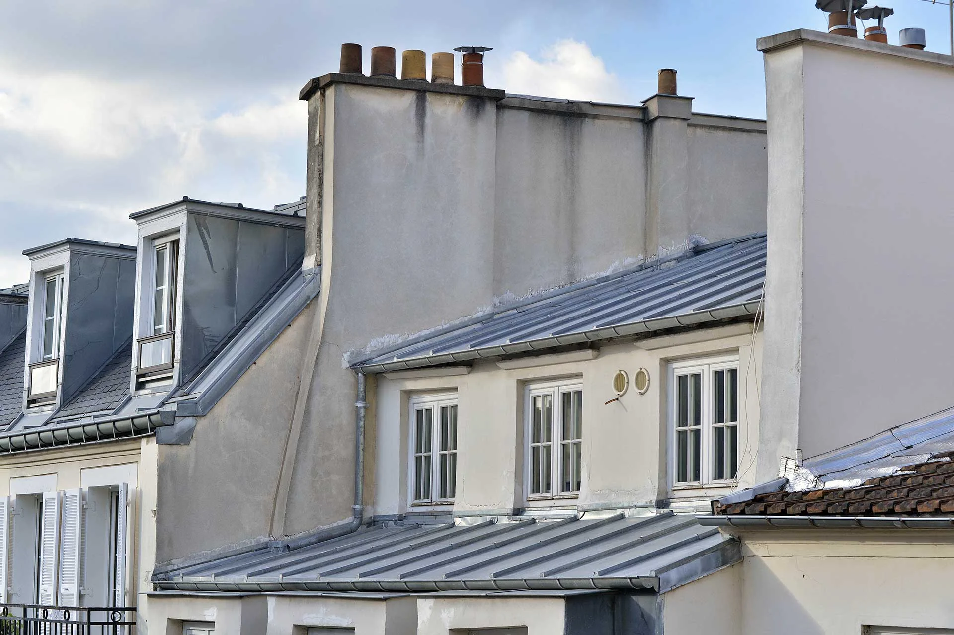 Façades d'immeubles haussmanniens et de l'hôtel Eugénie avec toits mansardés sous un ciel partiellement nuageux.